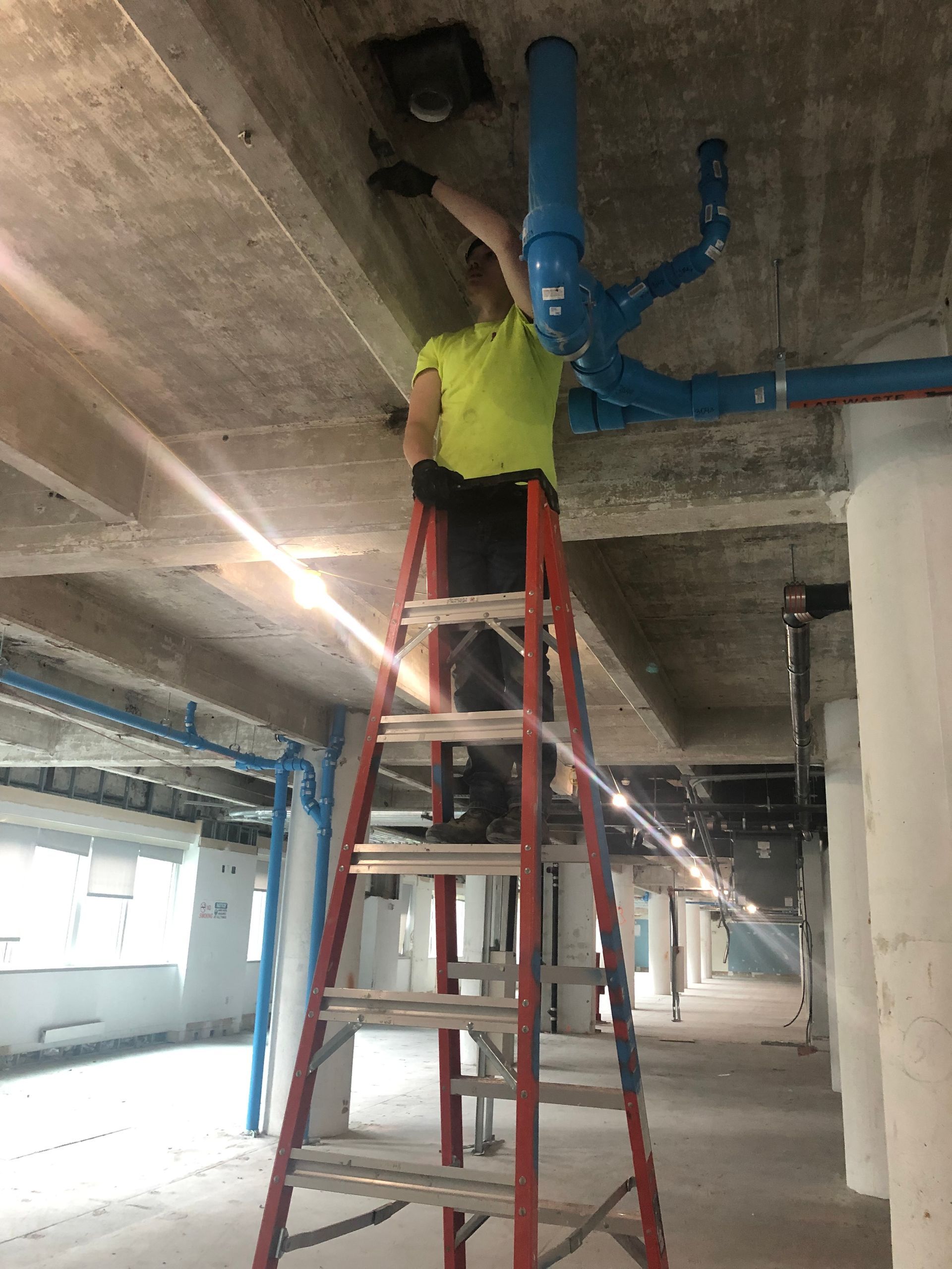 A man is standing on a ladder working on a pipe.