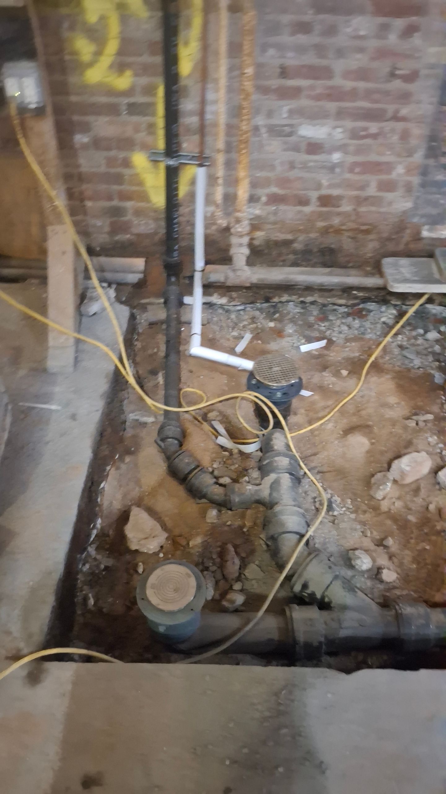 A bunch of pipes are laying in the dirt in a basement.