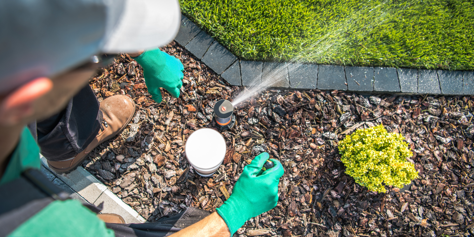 A man is working on a sprinkler in a garden.