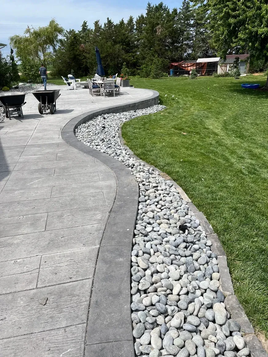 A Patio with A Concrete Walkway Surrounded by Rocks and Grass — Exeter, NE — Axline Landscaping & Trees