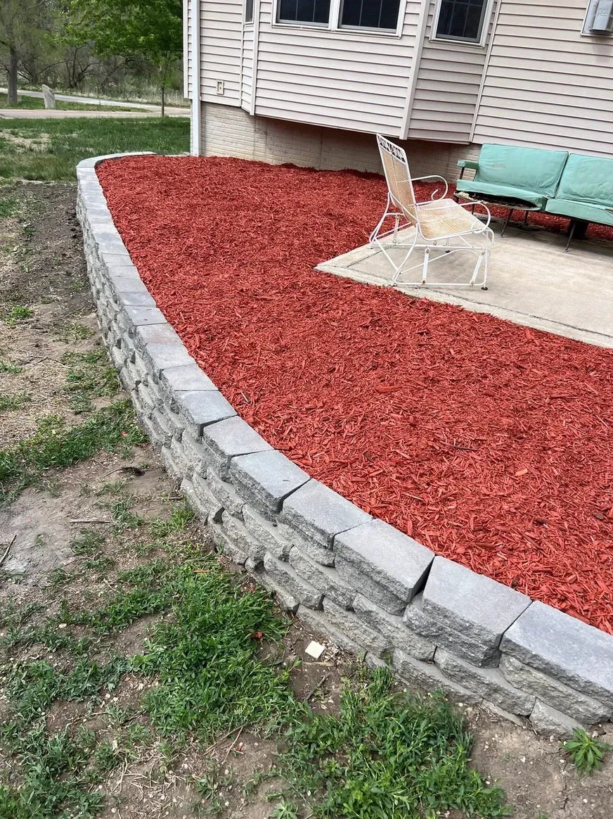 A Brick Wall Surrounded by Red Mulch Next to A House — Exeter, NE — Axline Landscaping & Trees