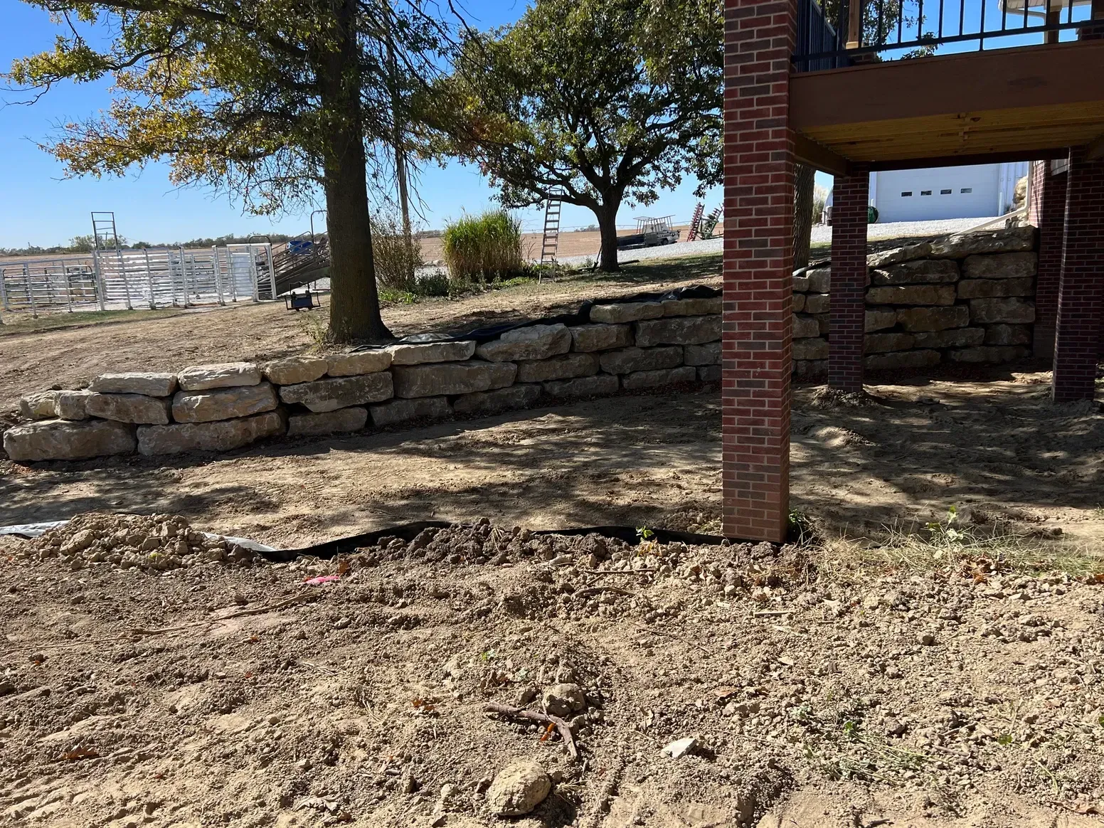 A Stone Wall Is Being Built Next to A Brick Building — Exeter, NE — Axline Landscaping & Trees