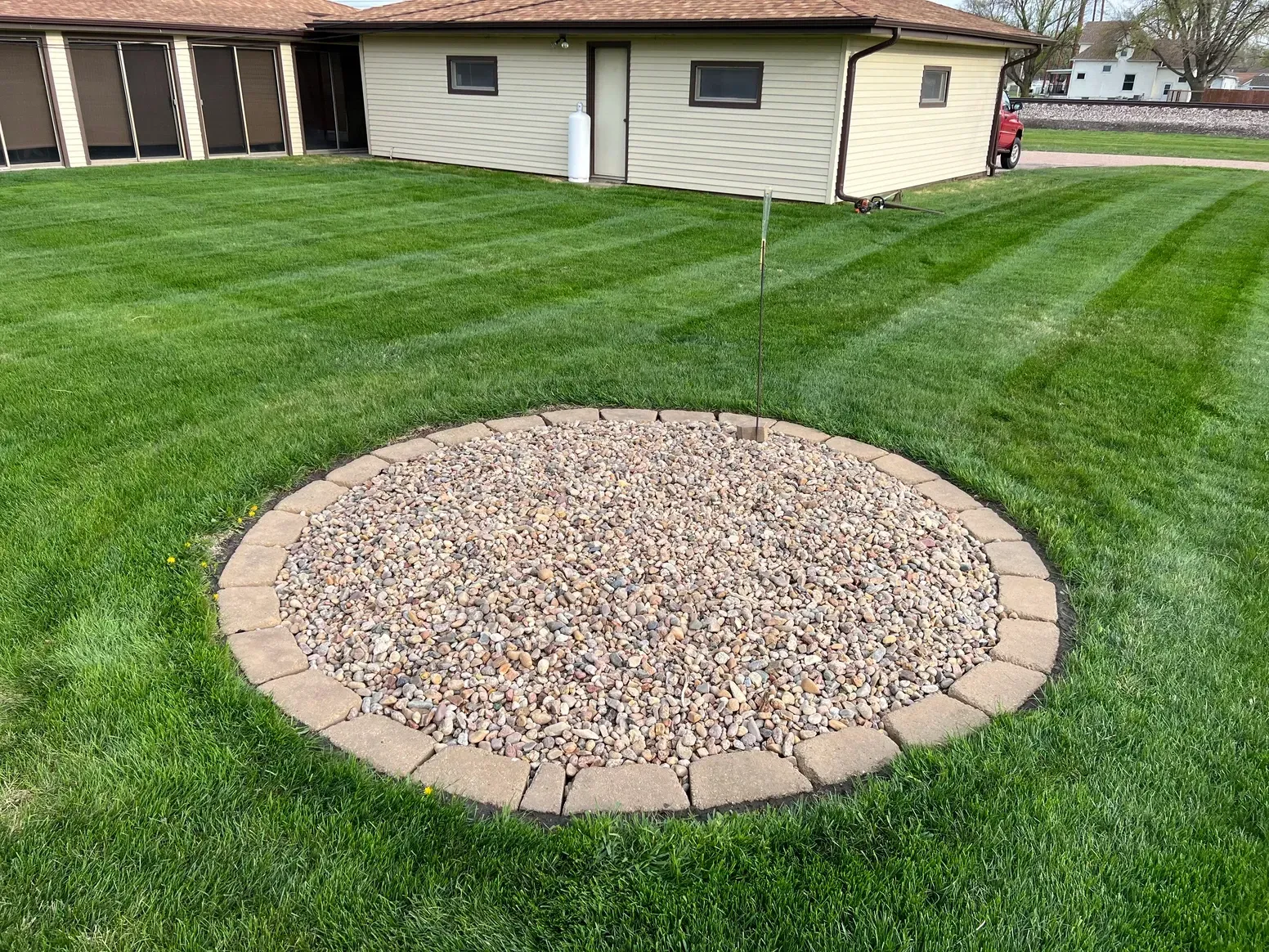 A Circular Stone Patio in The Middle of A Lush Green Lawn in Front of A House — Exeter, NE — Axline Landscaping & Trees