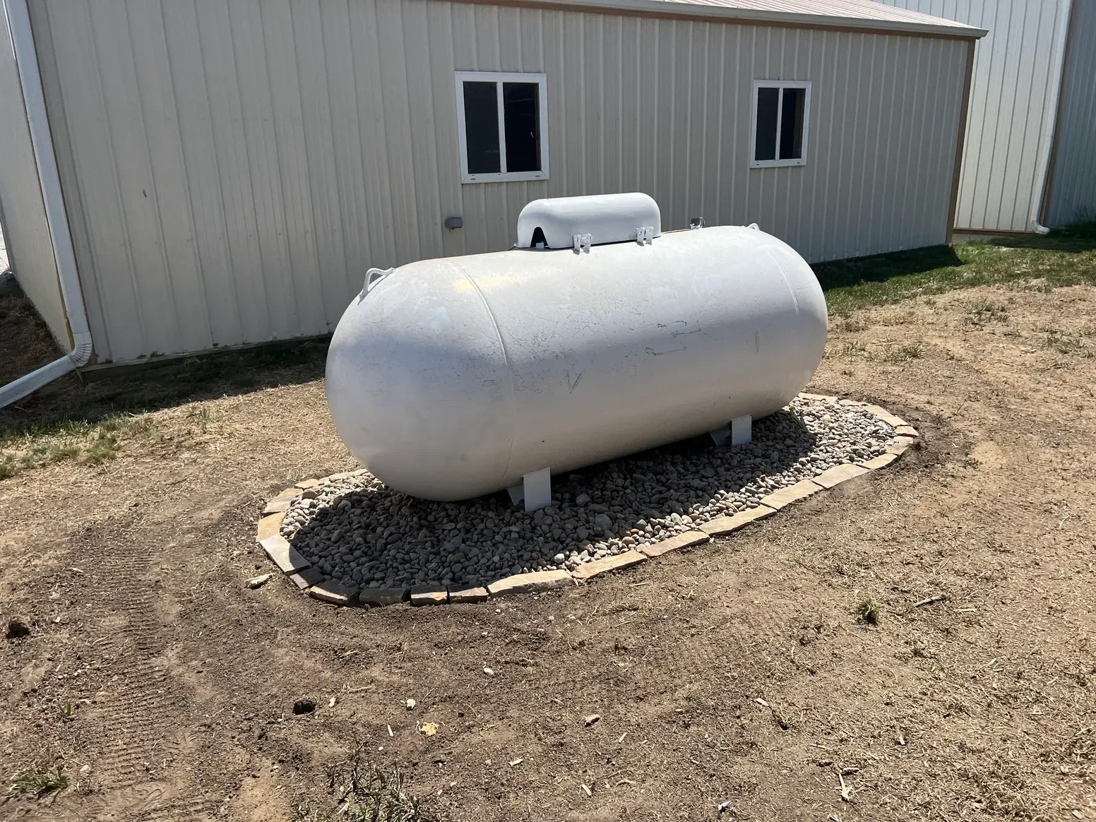 A Large White Propane Tank in The Dirt in Front of A Building — Exeter, NE — Axline Landscaping & Trees