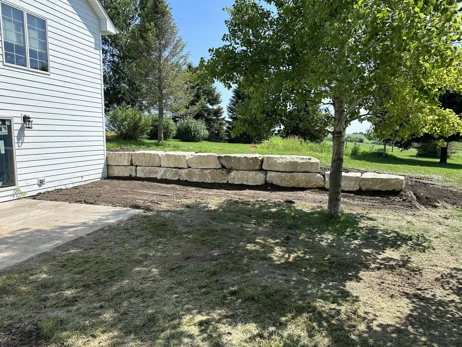 A Stone Wall Is Being Built in The Backyard of A House — Exeter, NE — Axline Landscaping & Trees