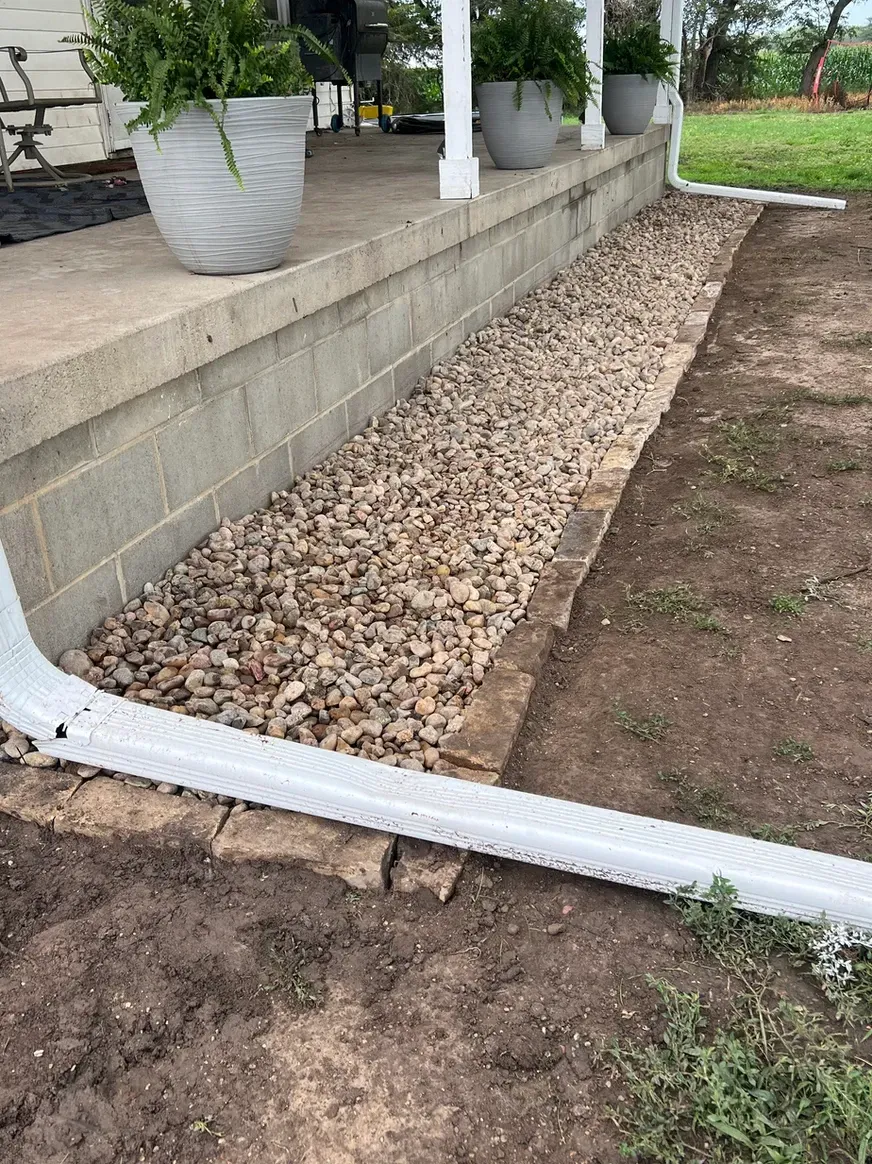 A White Gutter Is Sitting on The Ground Next to A Brick Wall — Exeter, NE — Axline Landscaping & Trees