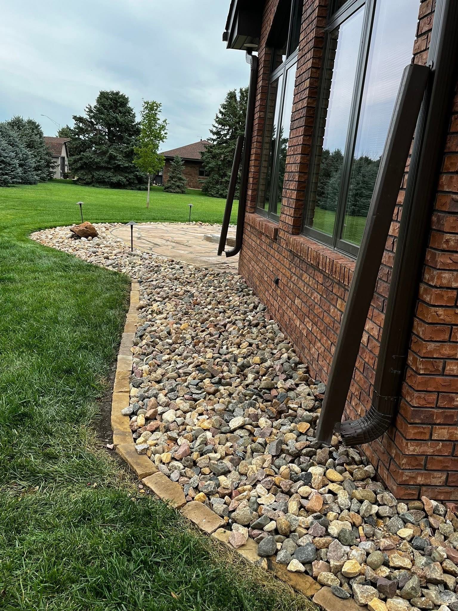 A brick house with brown gutters has a gravel bed along its foundation and adjacent lawn.
