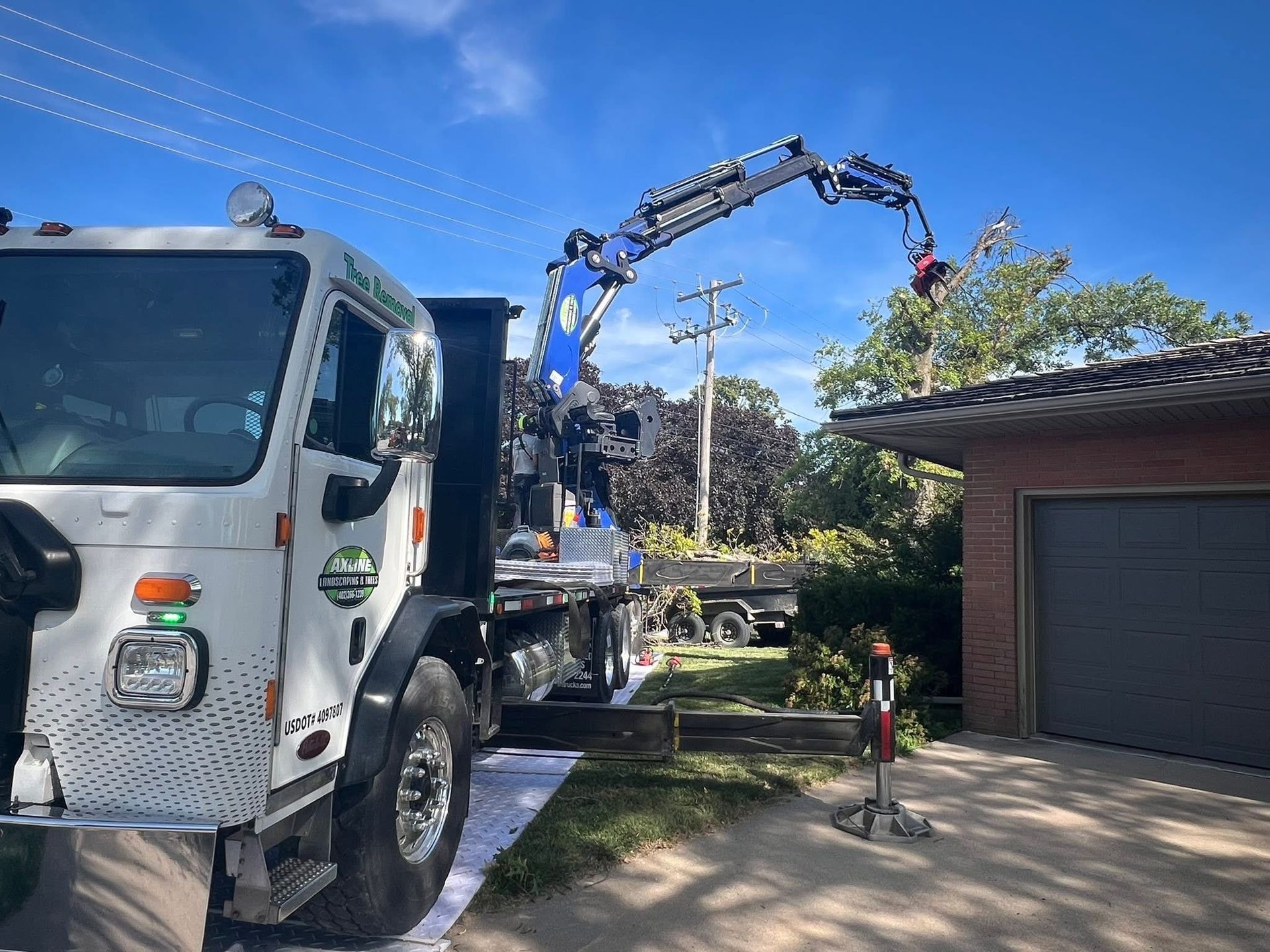 Truck with crane trimming tree near a house. Blue sky.
