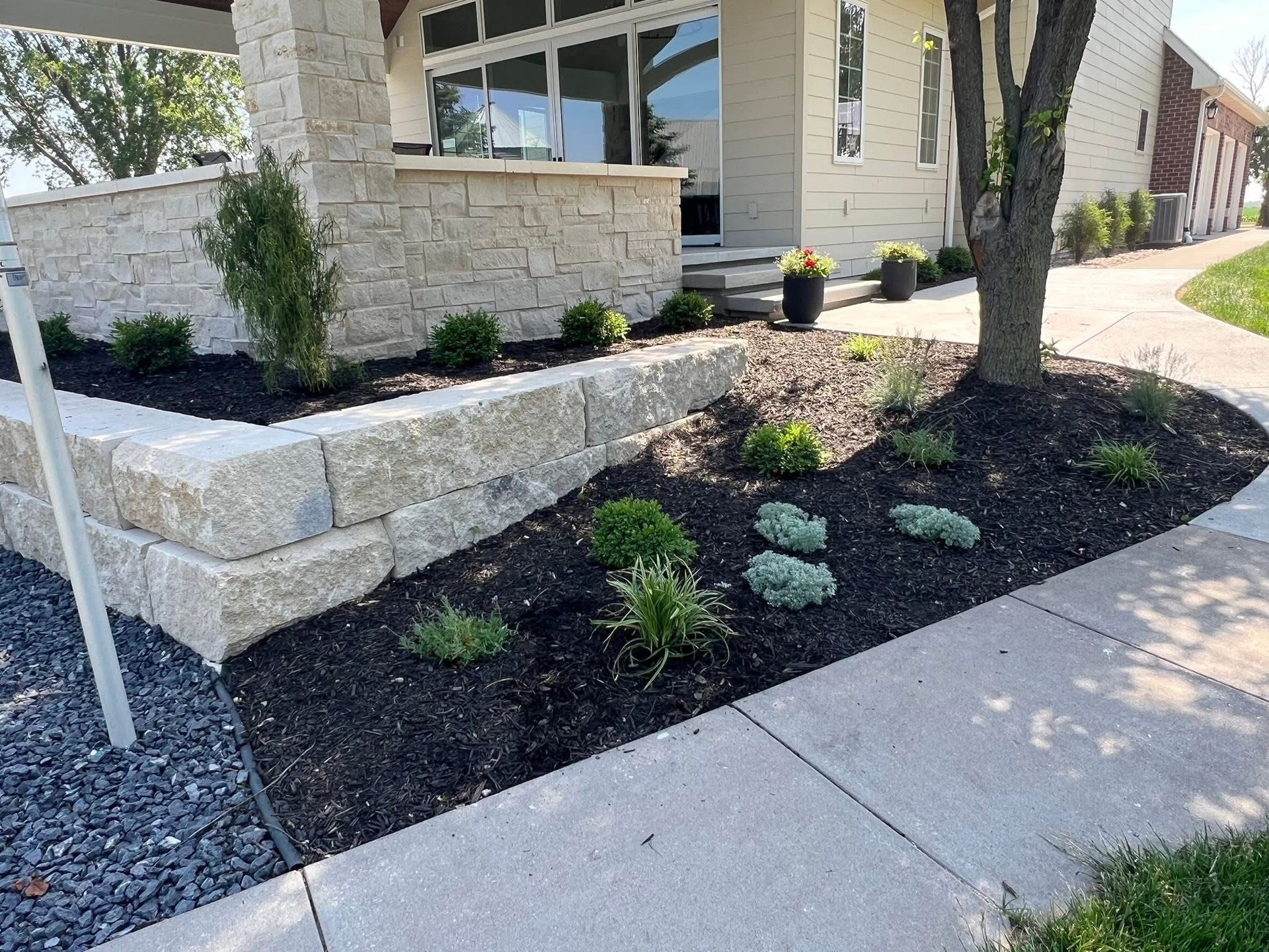 Landscaped yard with retaining wall, mulch, plants, and sidewalk.