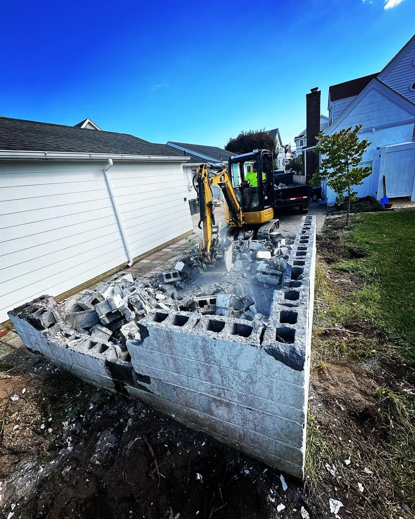 An excavator is demolishing a concrete block in front of a house