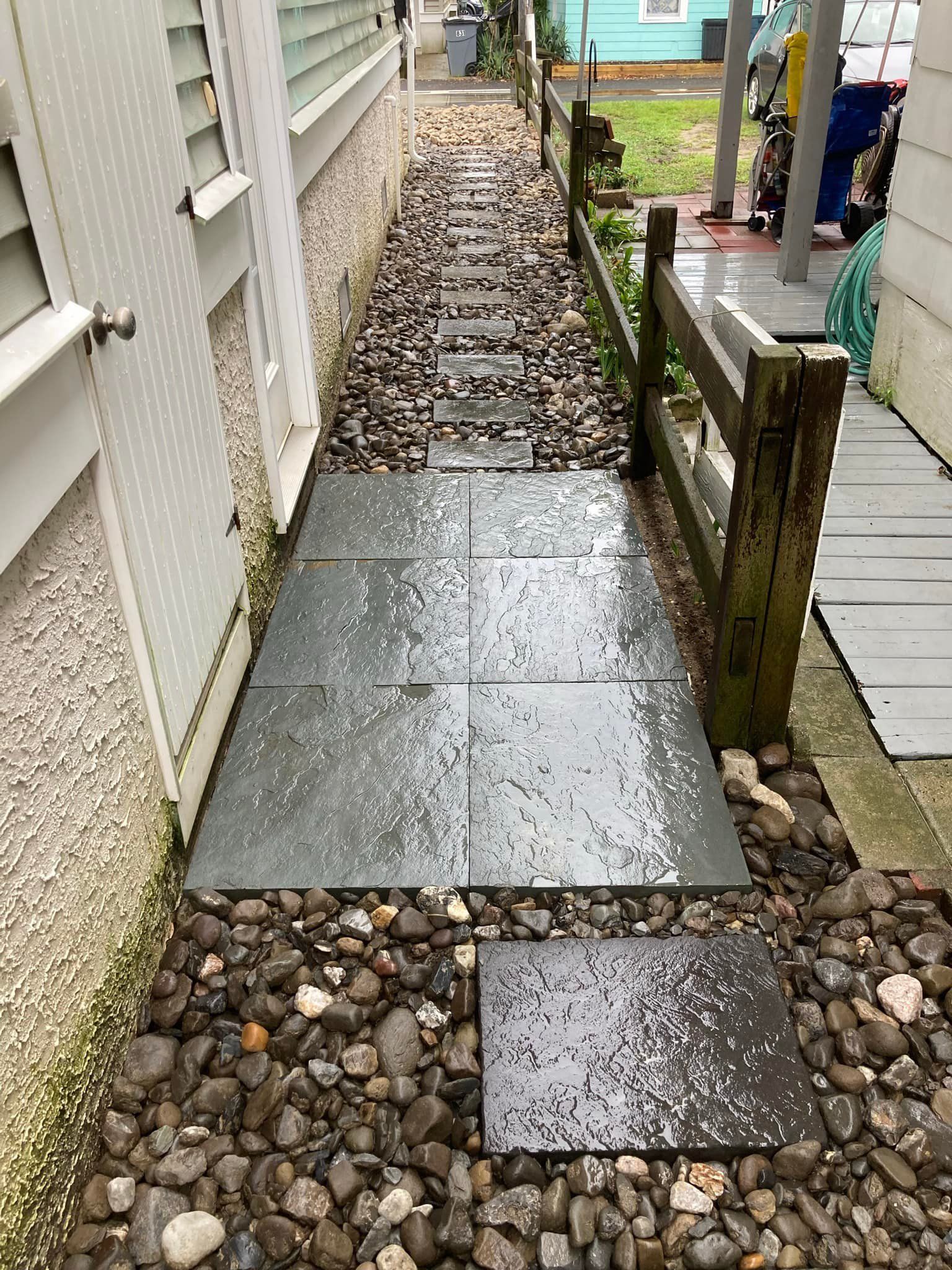 A stone walkway leading to a house with a wooden fence