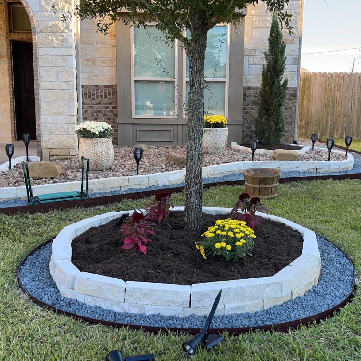 A tree in a circular planter with flowers in front of a house