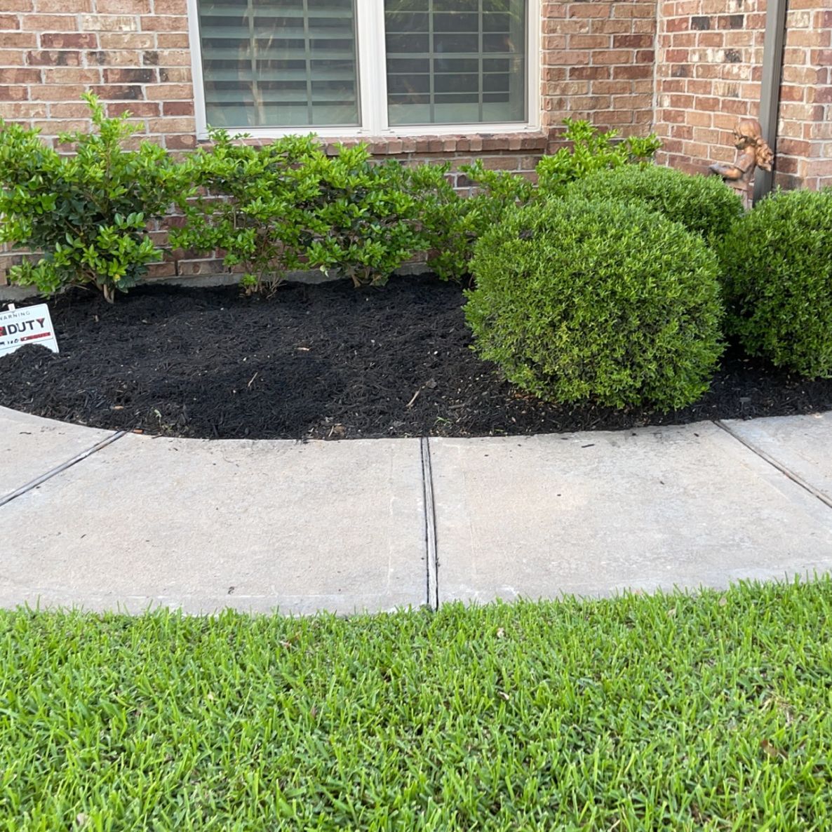 A brick house with a sidewalk and bushes in front of it