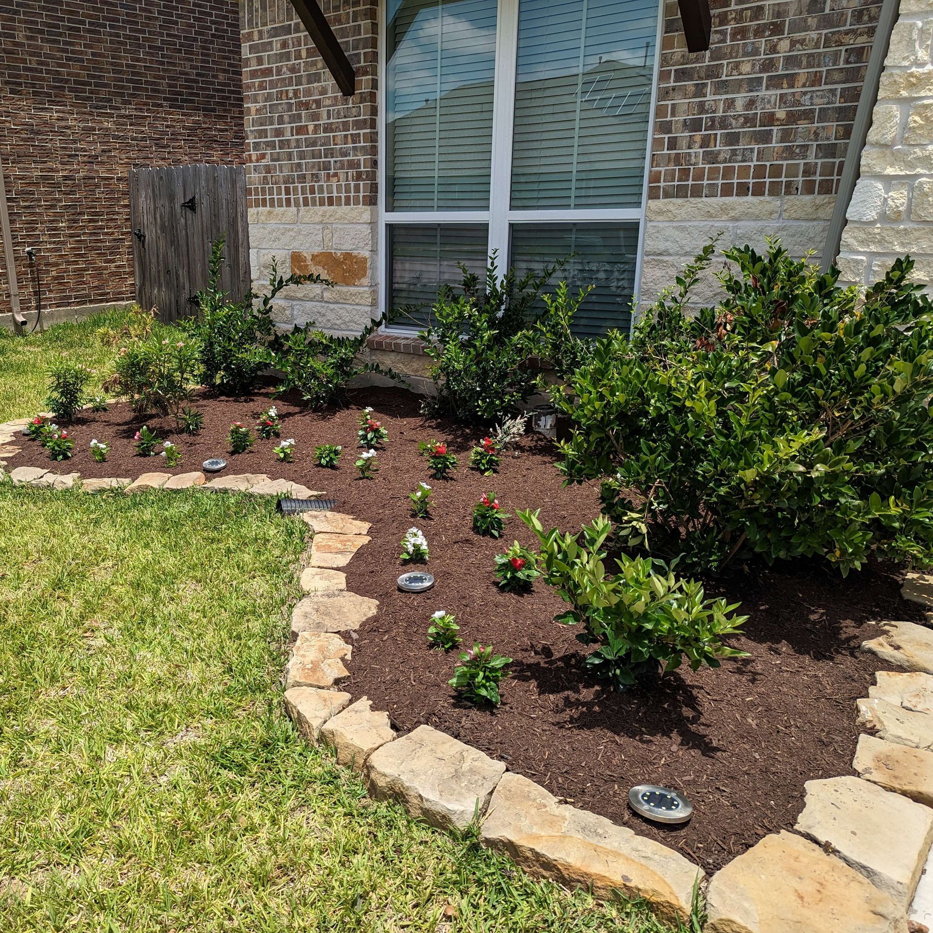 A garden with flowers and shrubs in front of a brick house.