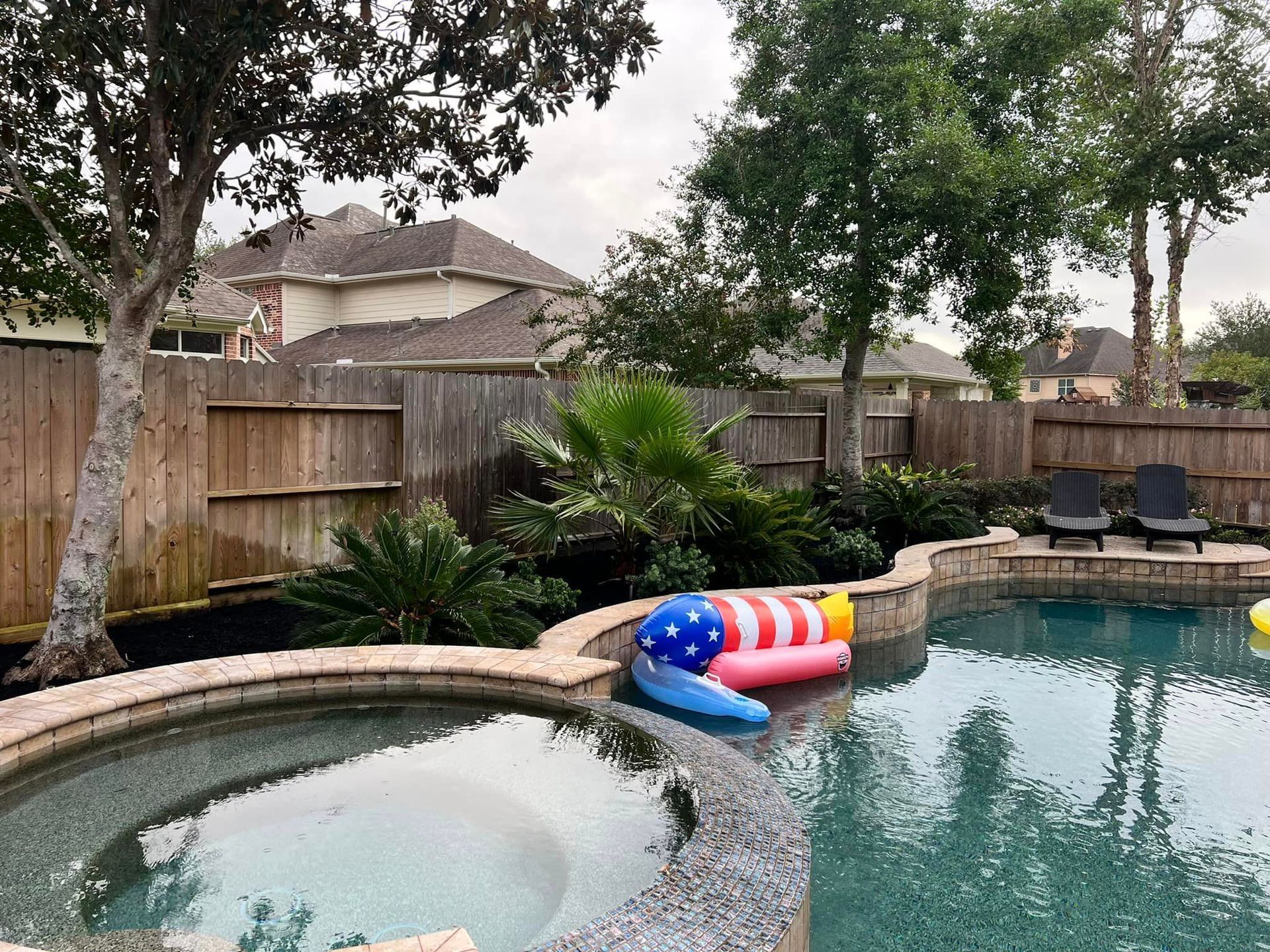 A large swimming pool surrounded by trees and a wooden fence.