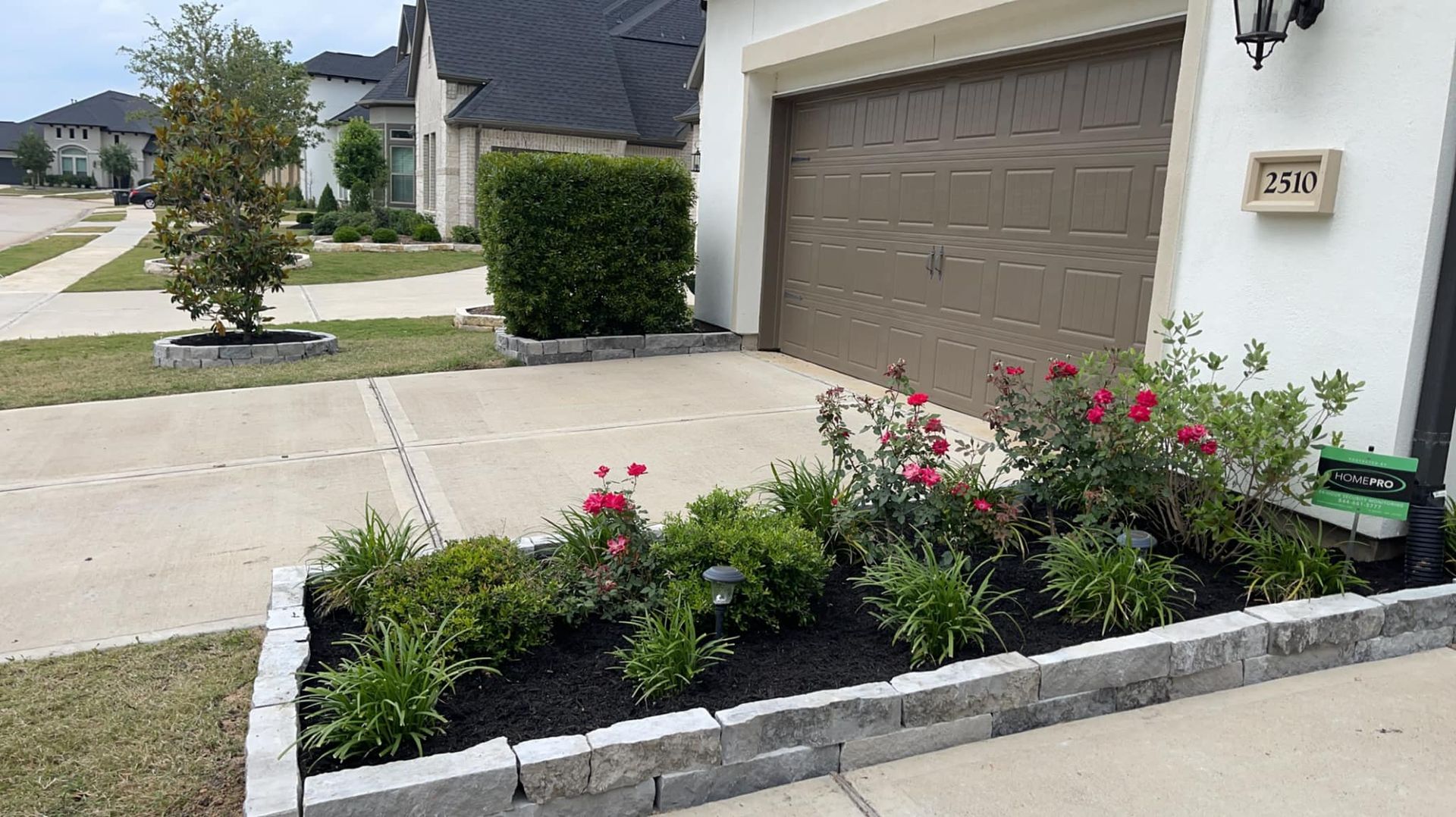 A white house with a brown garage door and a garden in front of it.
