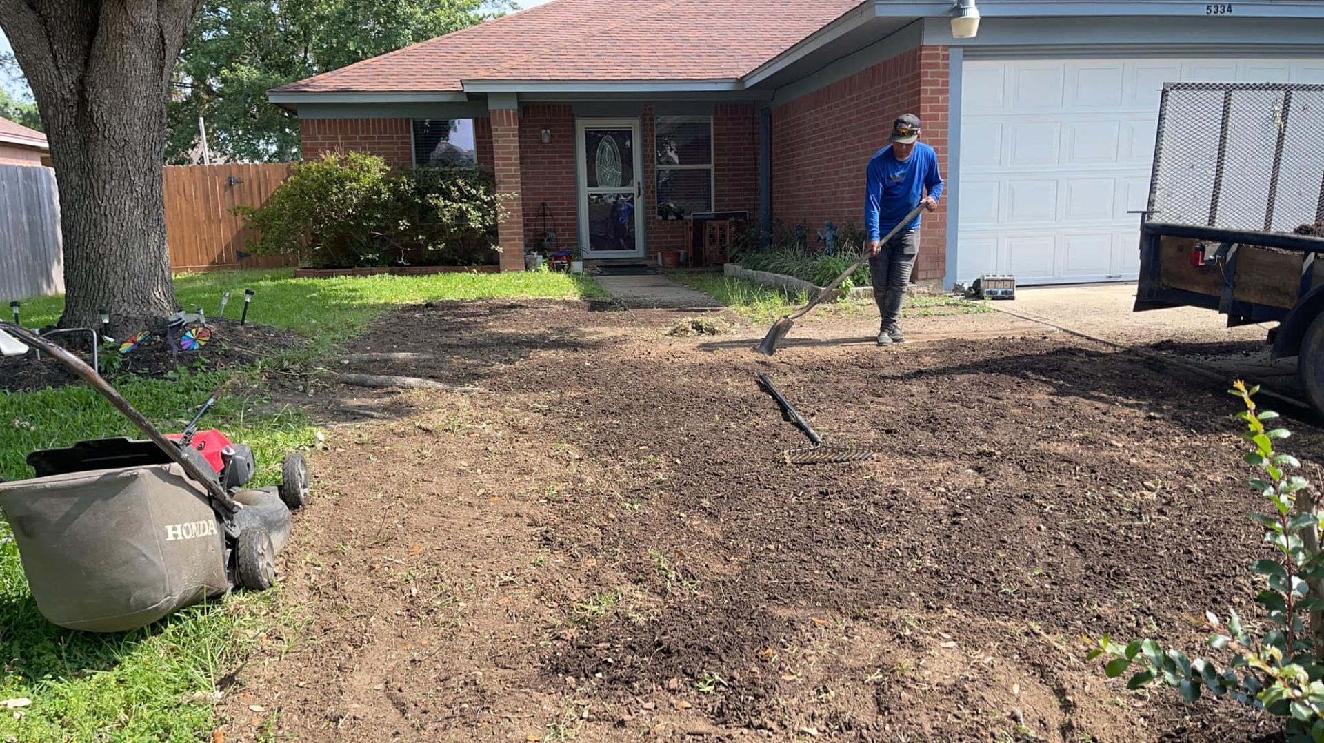 A man is raking dirt in front of a house.