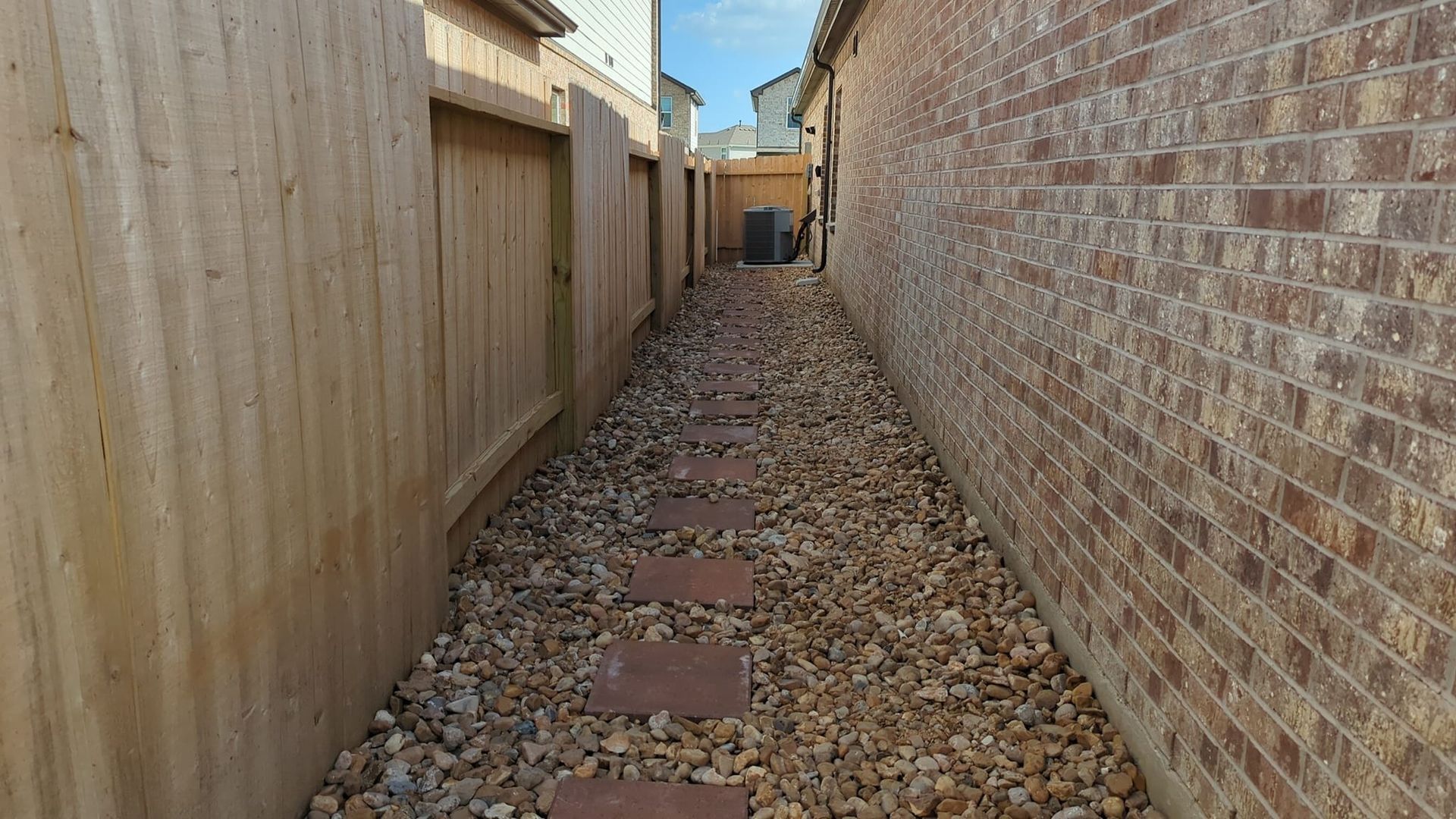 A stone walkway between two brick buildings with a wooden fence.
