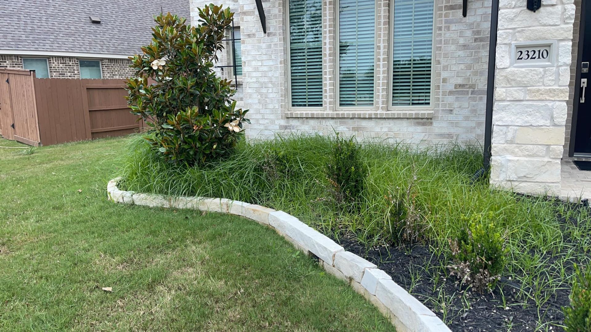 A white brick house with a lush green lawn in front of it.