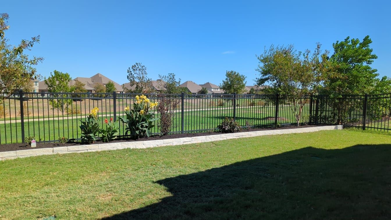 A fence surrounds a lush green yard with trees and bushes.