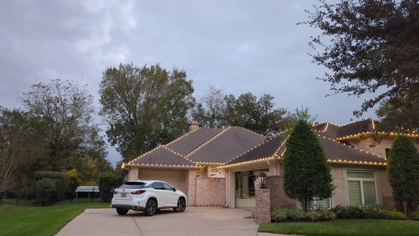 A white suv is parked in front of a house with christmas lights on the roof.