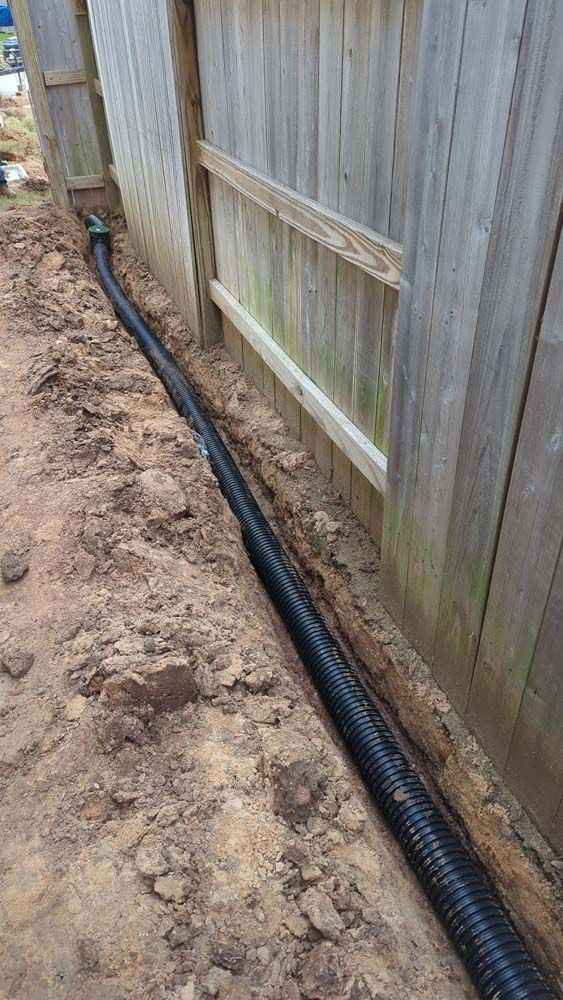 A drain pipe is being installed next to a wooden fence.