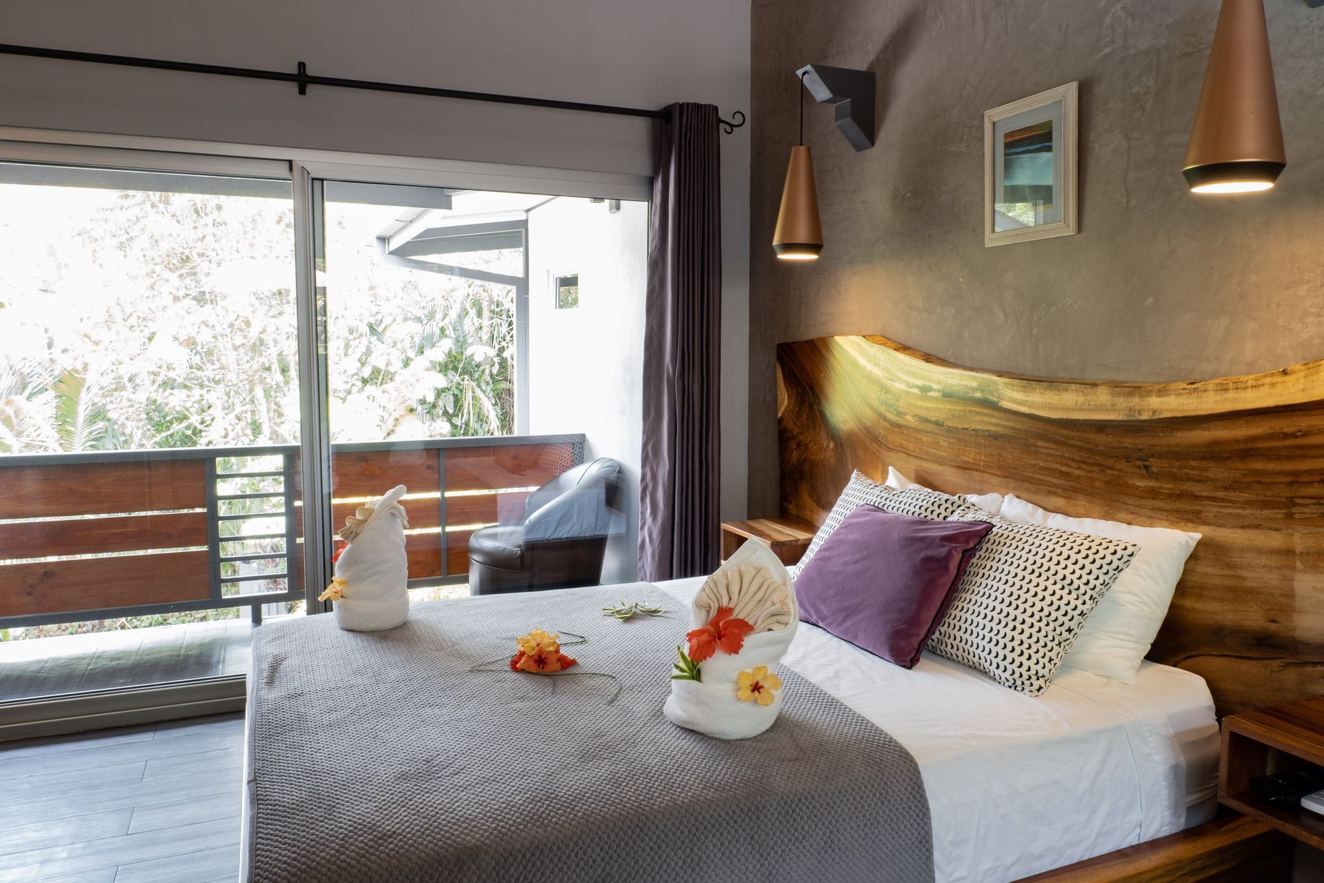 A hotel room featuring a queen-sized bed with a rustic live-edge wood headboard, a sliding glass door, and a private deck.