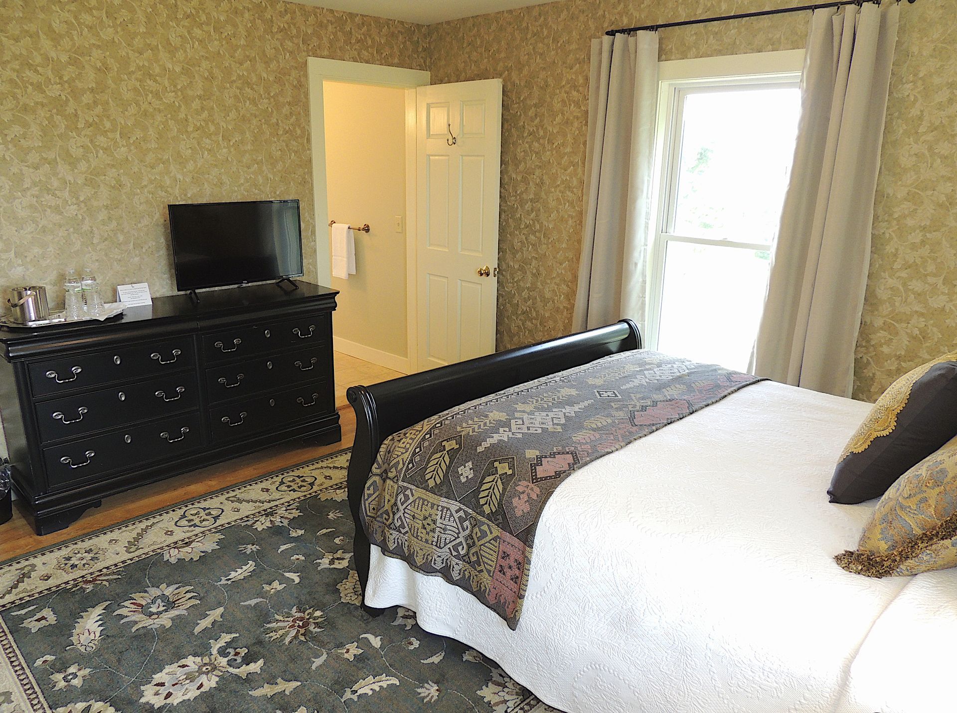 A bedroom with a bed , dresser , television and window.