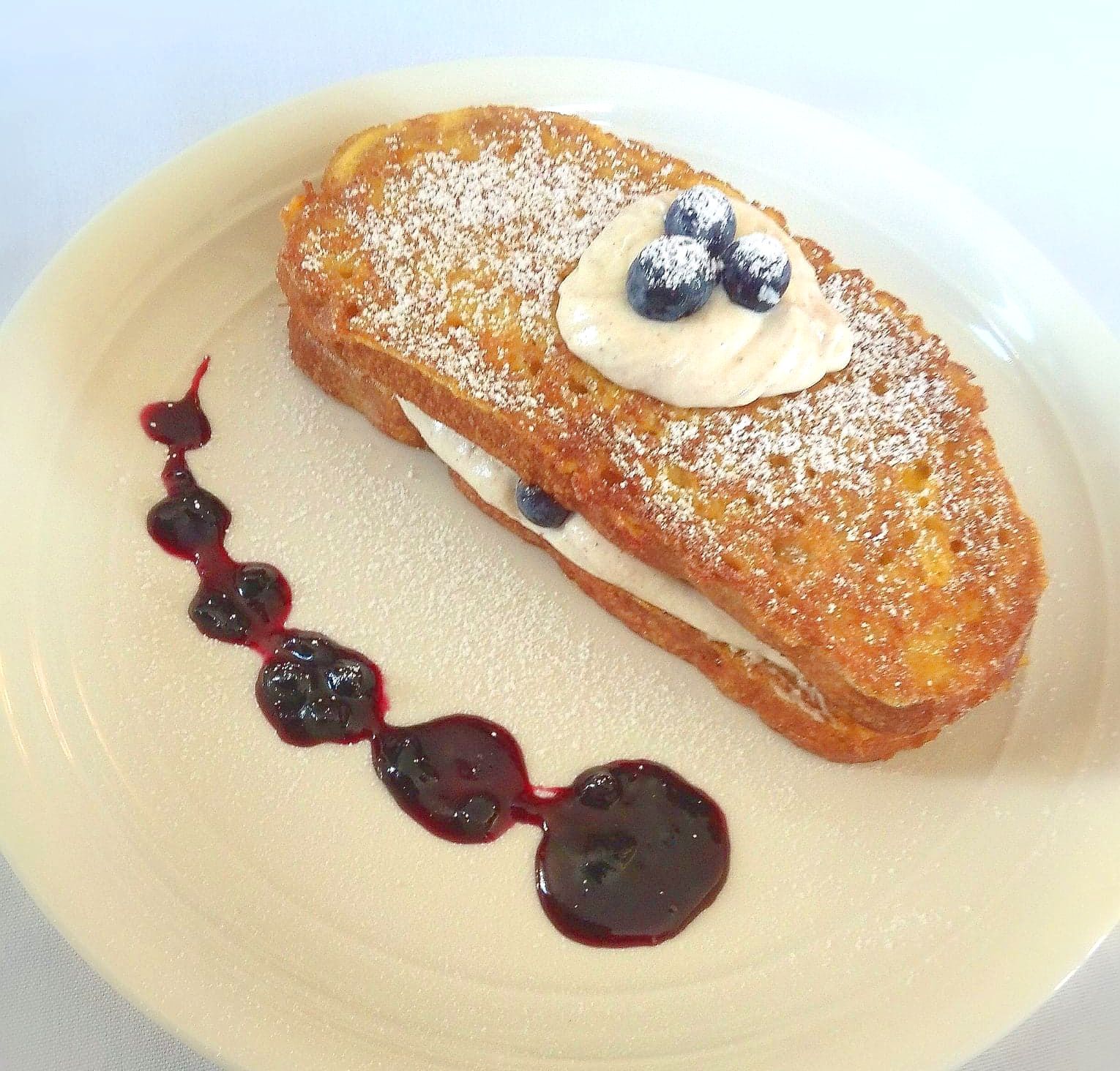 French toast with whipped cream and blueberries on top on a white plate