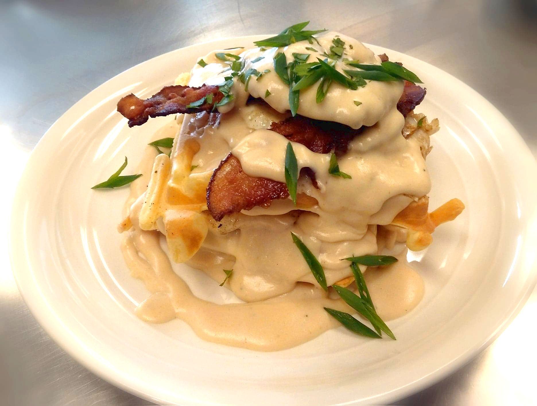 A white plate topped with a stack of food with bacon and cheese