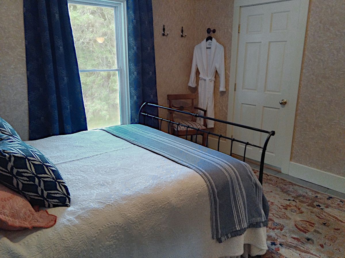 A bedroom with a bed , chair , window and a robe hanging on the wall.