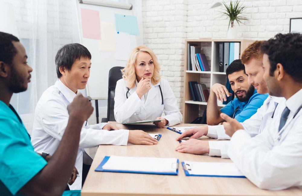 A group of doctors from different races is meeting at a table. They are in the clinic. They discuss the results of the patient's tests. They have a medical consultation