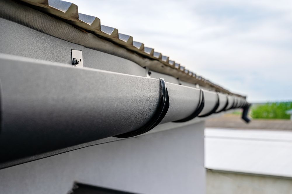 Dark Gray Rain Gutter Along a White Building, With a Cloudy Sky Background — Coffs Coast Roofing In Mullaway, NSW
