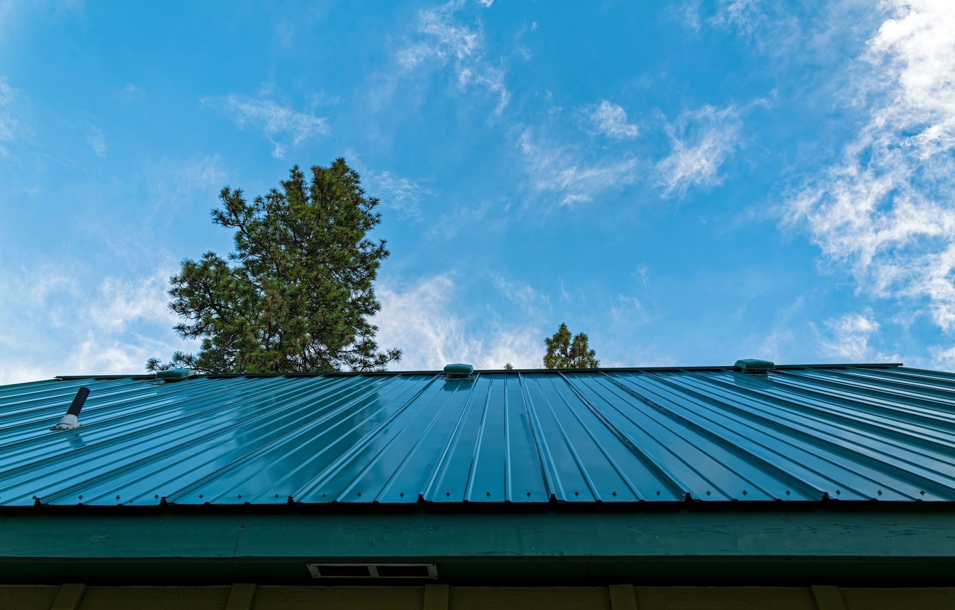 Blue Metal Roof Against a Bright Blue Sky With Wispy Clouds, Trees in the Background — Coffs Coast Roofing In Bellingen, NSW