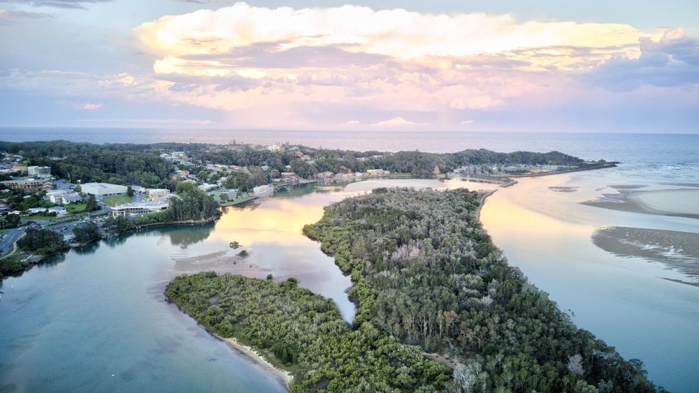 Aerial View of Coastal Landscape at Sunset, Water, Trees, and Buildings Under a Sky — Coffs Coast Roofing In Nambucca, NSW