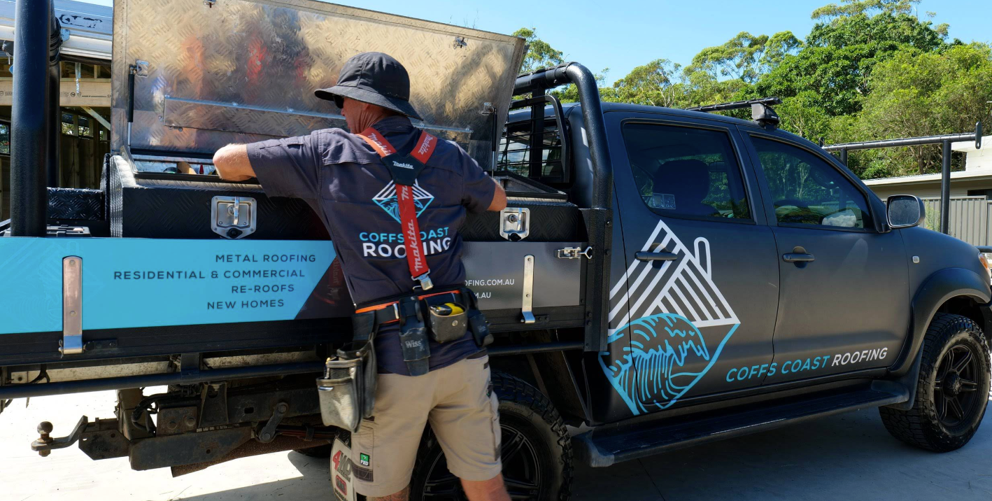 Man in work attire leaning on a black work truck with company logo.