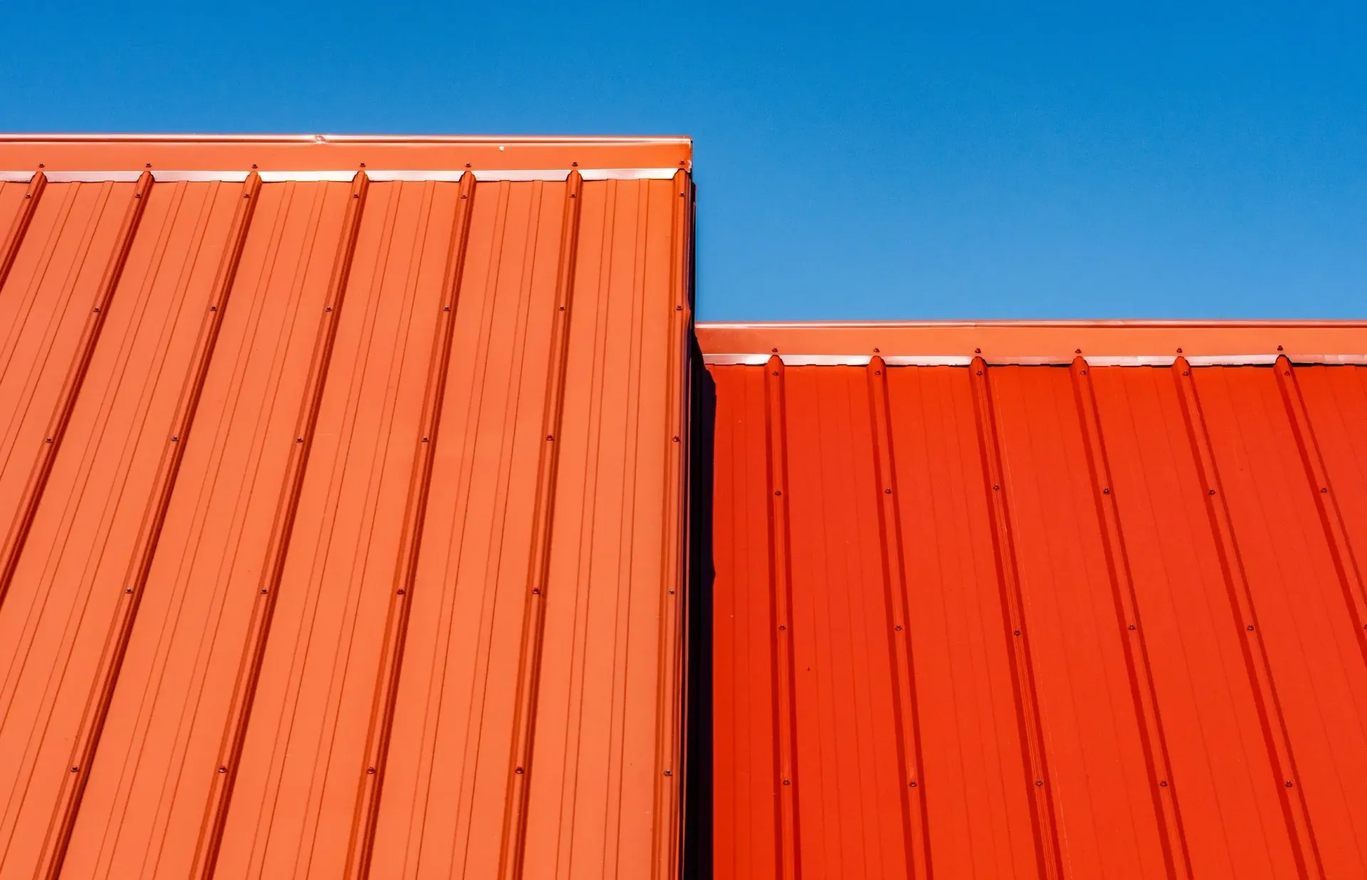 Two red metal roofs against a bright blue sky.
