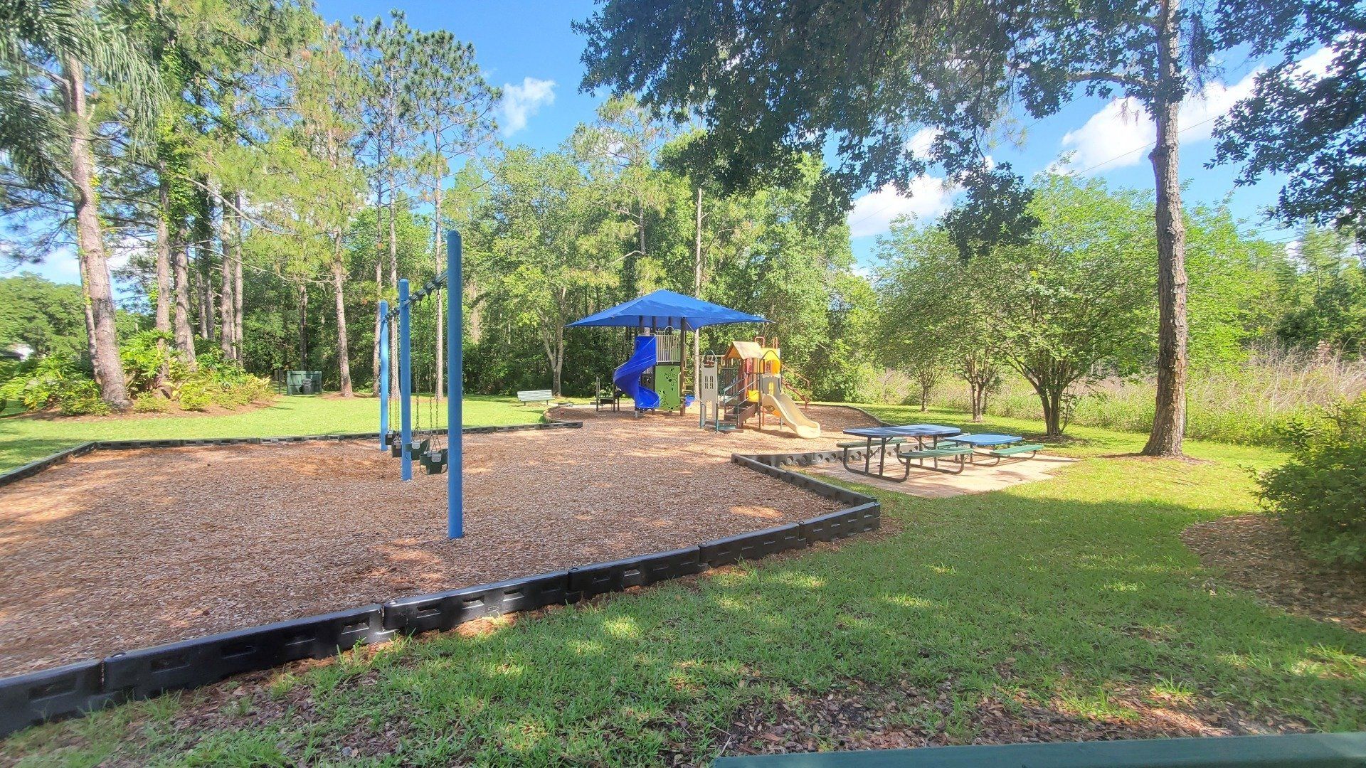 There is a playground with a blue umbrella in the middle of the park.