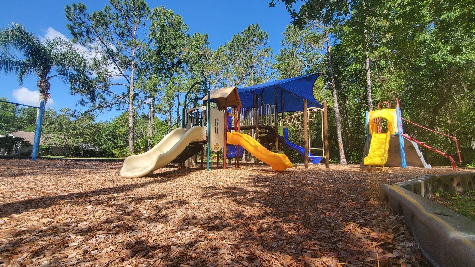 A playground with a slide and swings in a park surrounded by trees.