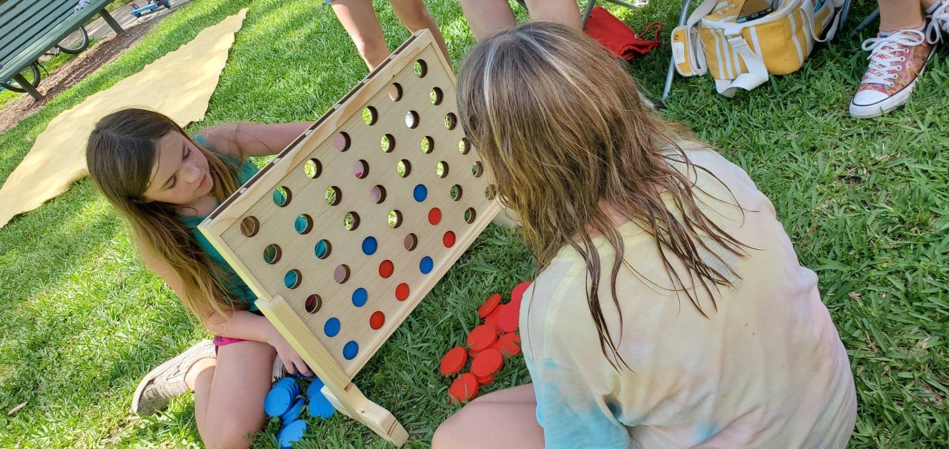 A group of young girls are playing a game of connect four in the grass.