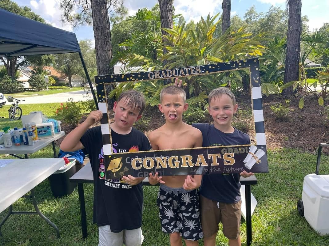 Three young boys are posing for a picture with a congratulations sign.