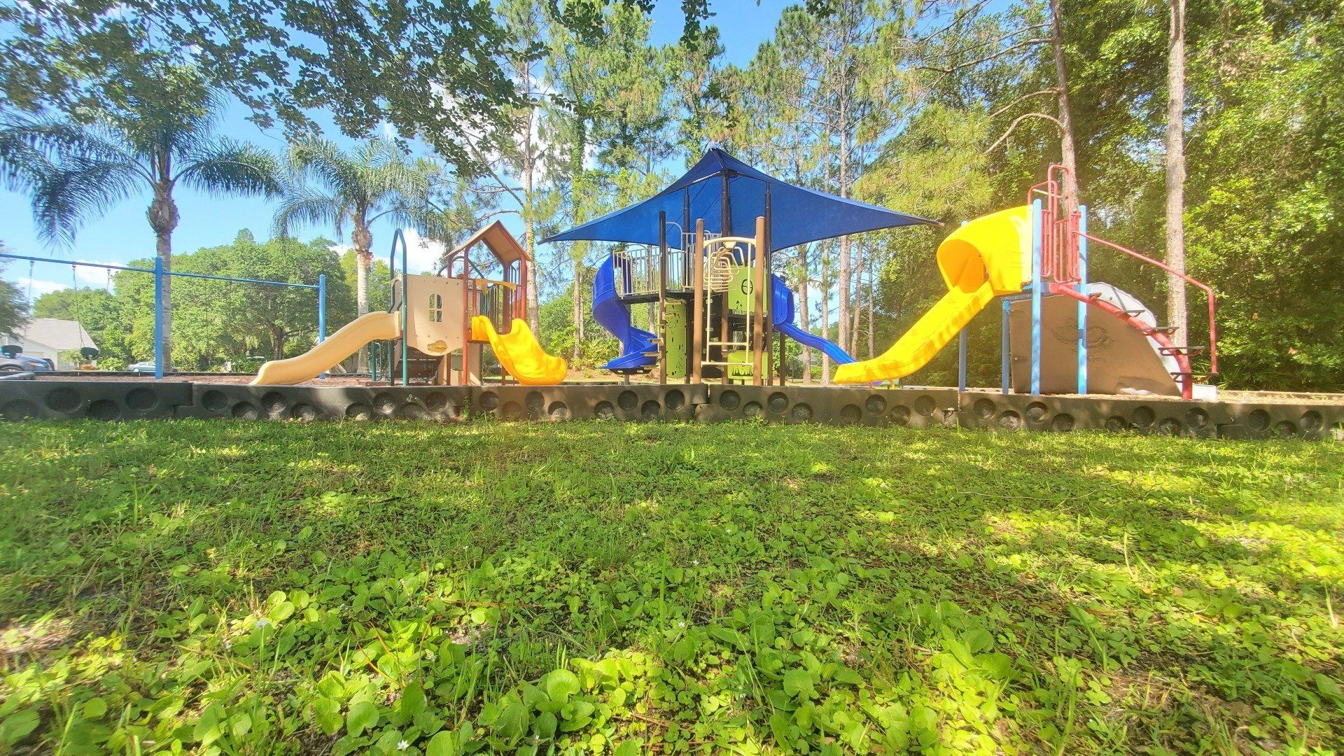 A playground with a slide and a blue umbrella in a park.