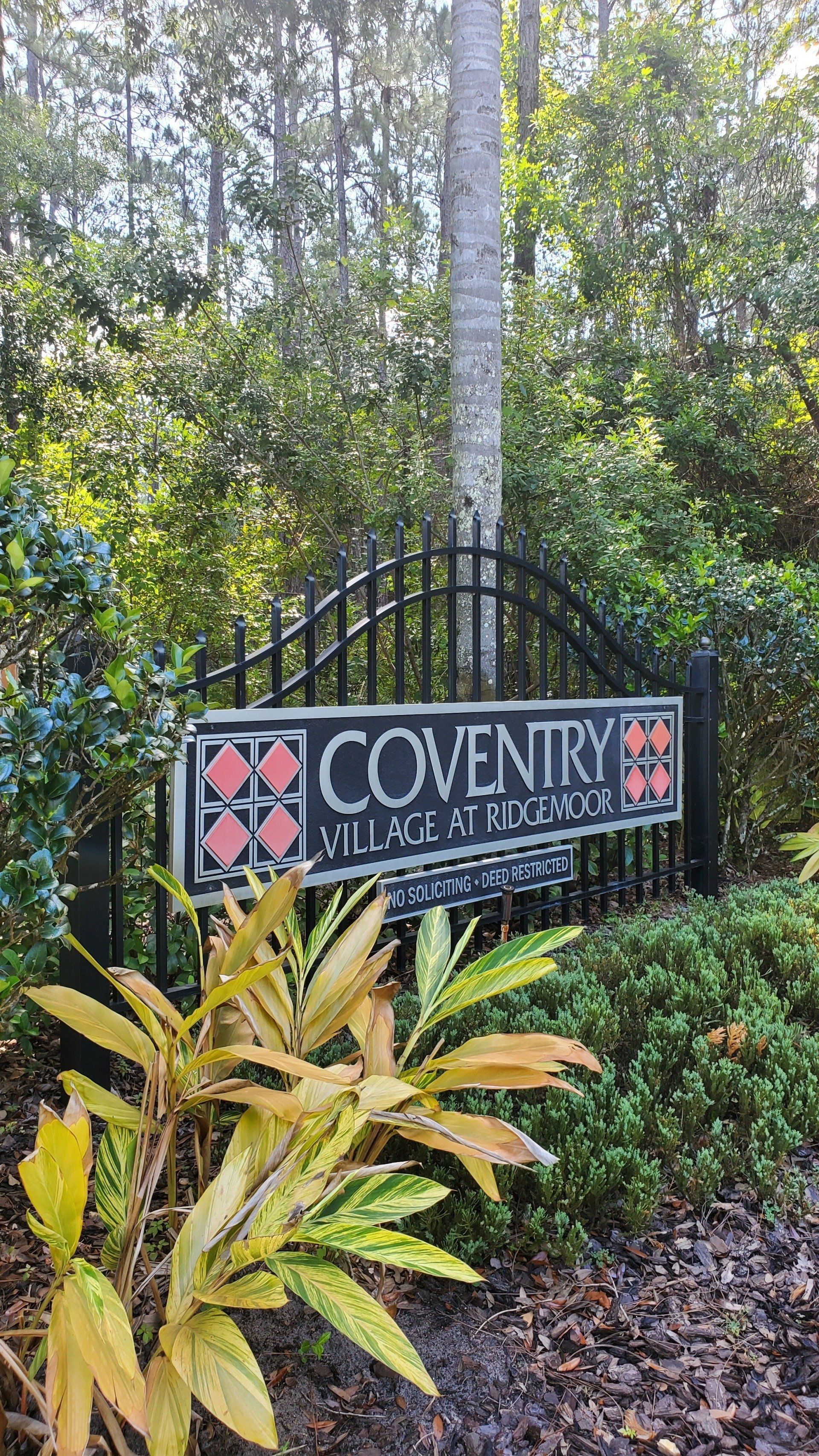 A sign is sitting on top of a fence in front of a lush green forest.