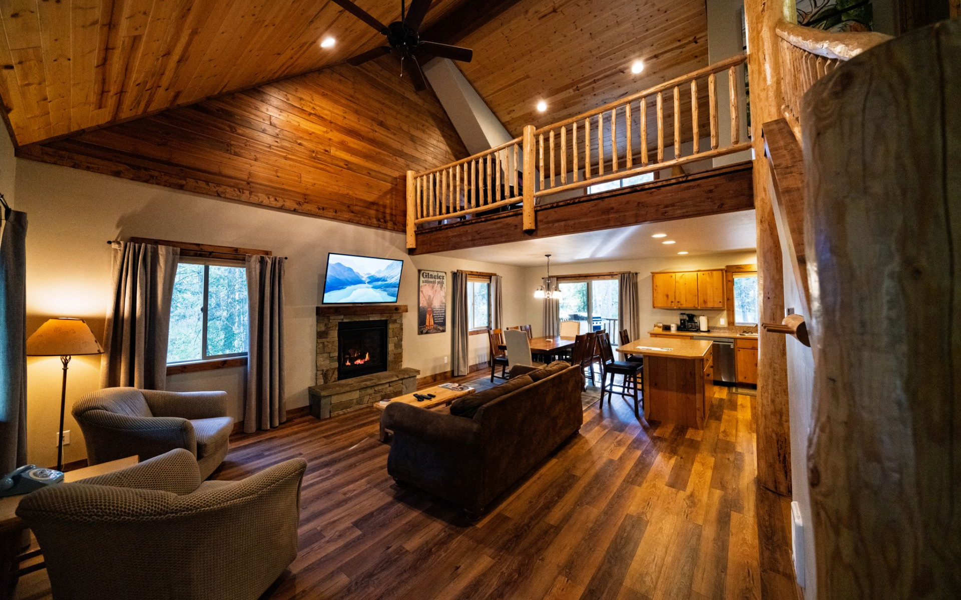 Cozy cabin interior with a fireplace, loft, and wooden beams.