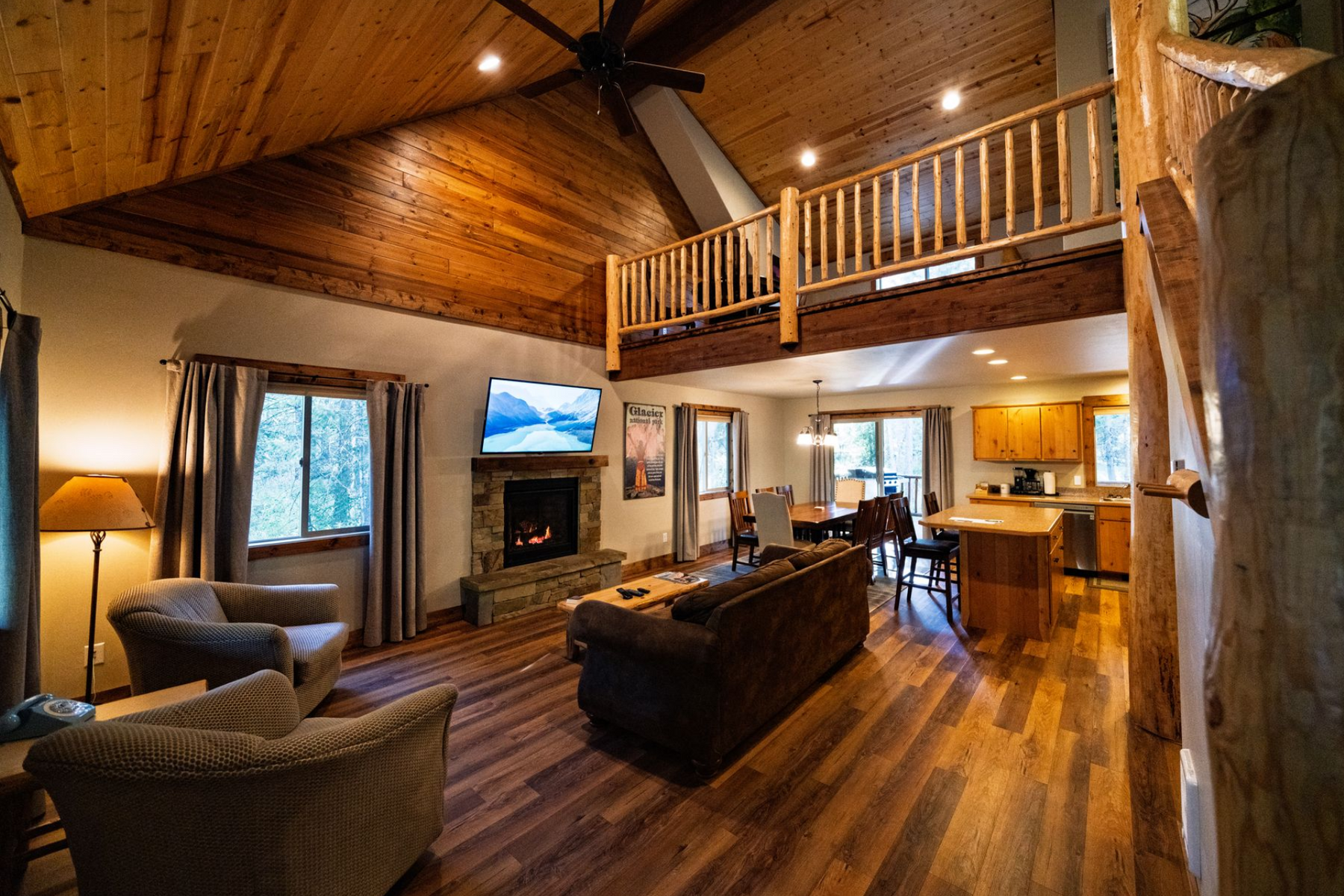 Cozy cabin interior with a fireplace, loft, and wooden beams.