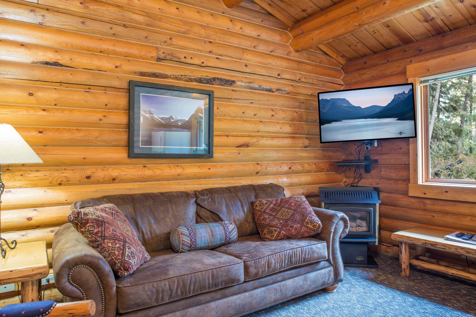 A living room in a log cabin with a couch , television and fireplace.