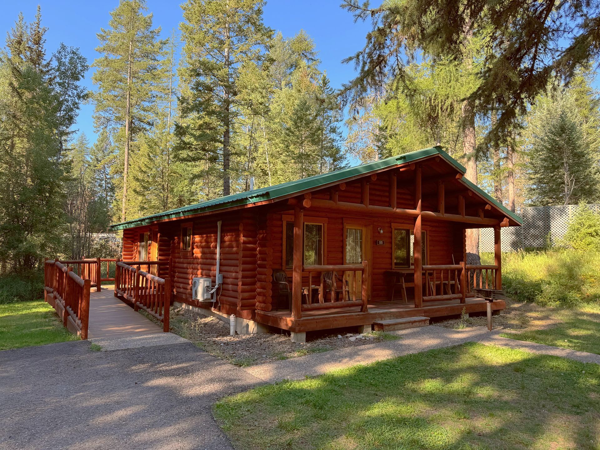 A small log cabin with a green roof is surrounded by trees.