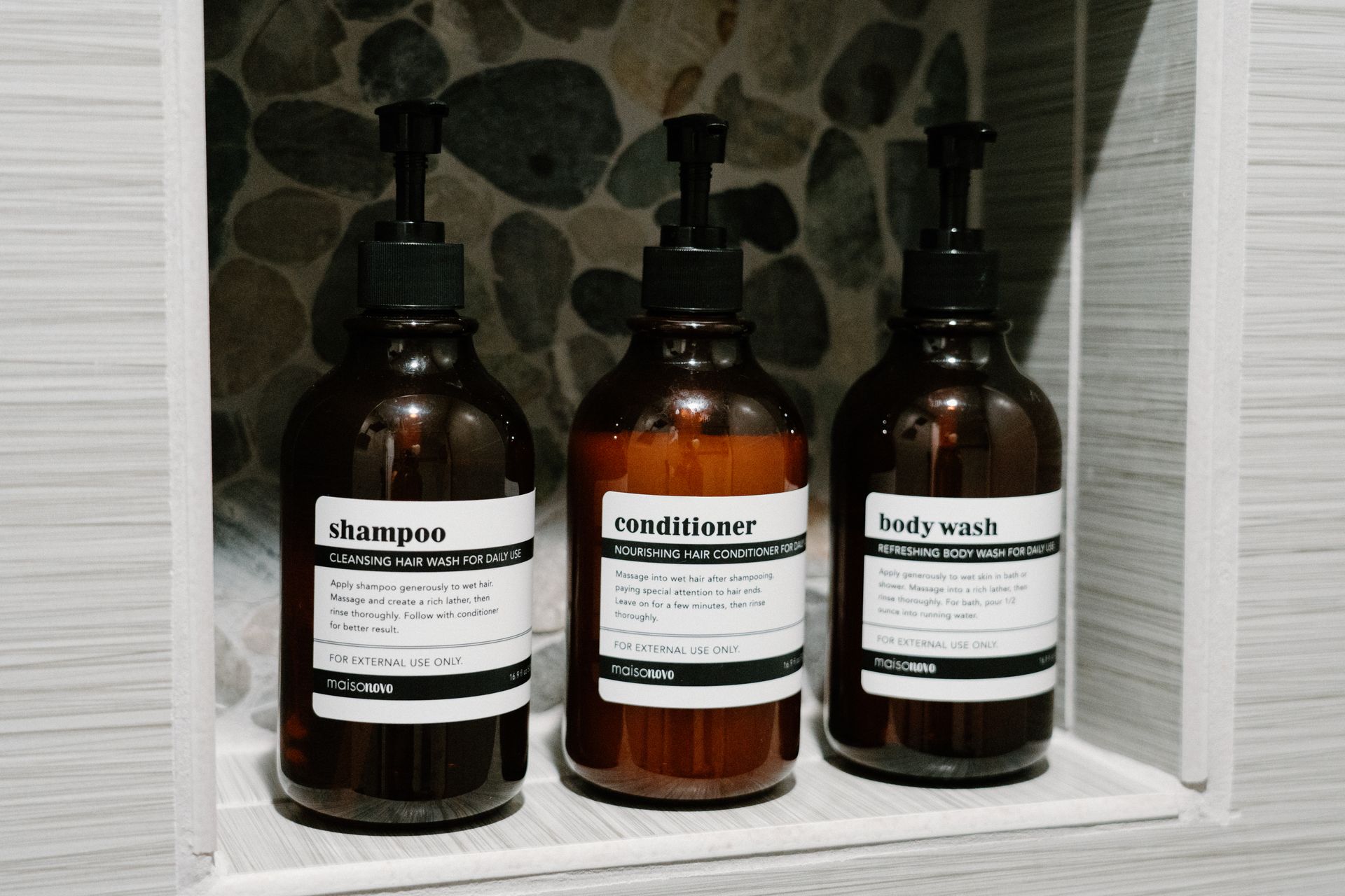Three bottles of shampoo , conditioner , and body wash are sitting on a shelf in a bathroom.