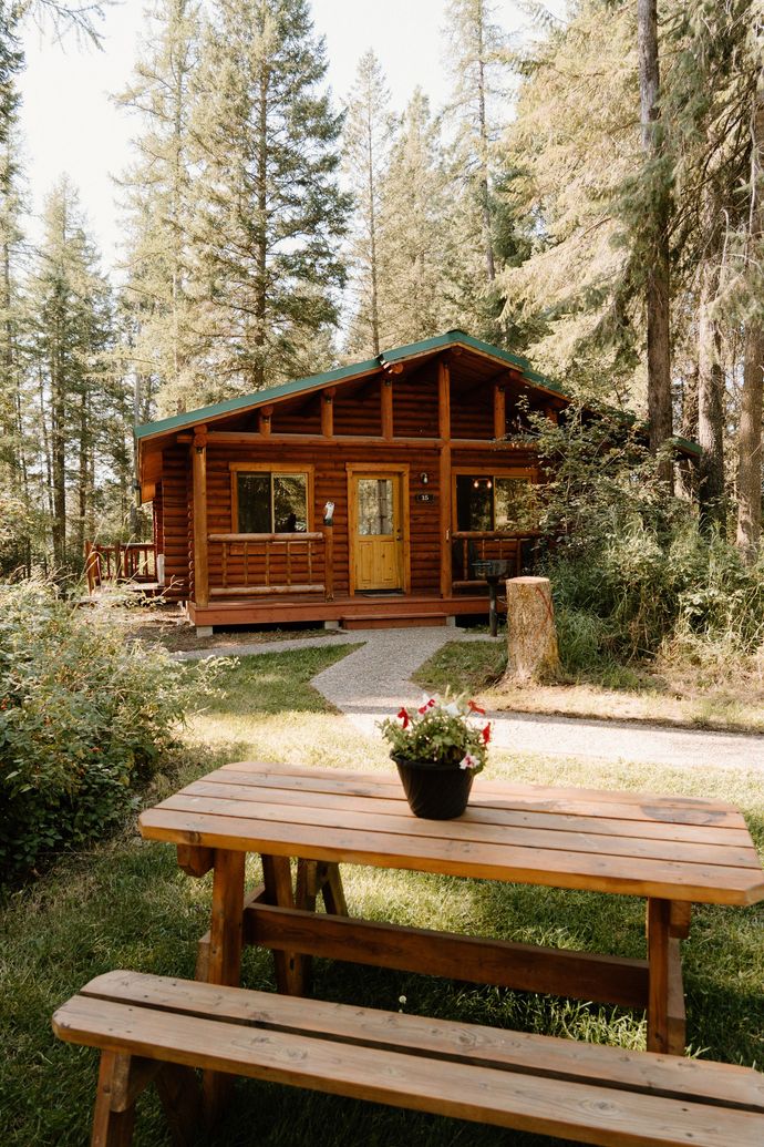 A wooden cabin in the woods with a picnic table in front of it.