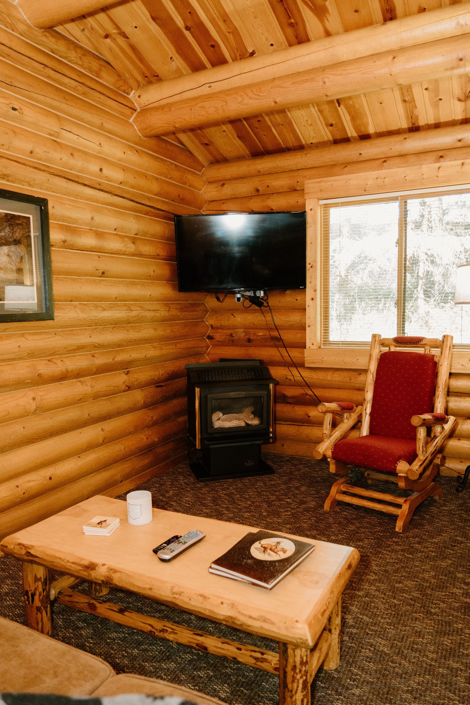 A living room in a log cabin with a table , chair , television and fireplace.